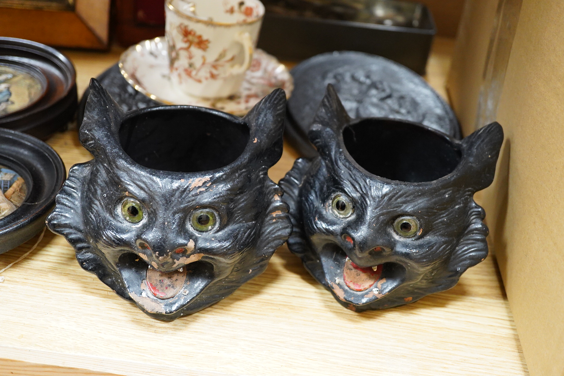 Two framed pot lids, two oval figural plaques,a moustache cup and saucer, two Bretby cats, framed print and mixed nut crackers cutlery etc